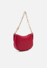 Sac à main en cuir rouge de forme arrondie, doté d'une bandoulière en chaîne dorée et d'une fermeture éclair. Texture lisse avec des détails minimaux.