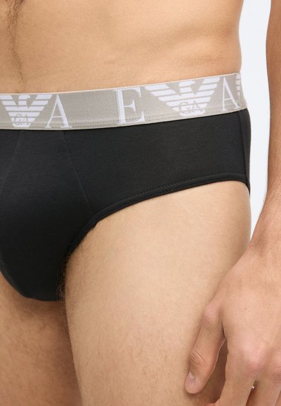 Fekete pamut boxeralsó világosszürke elasztikus derékpánttal, amely logót és csíkmintát ábrázol. Közeli kép a derékpánt dizájnjáról.