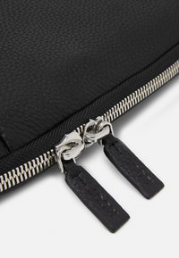 Zwarte leren clutch met een geplaveide textuur, voorzien van een zilveren rits met dubbele trekker en reliëf zwarte leren accenten.