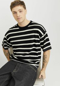 Sort og hvid stribet kortærmet skjorte med rund halslinje, parret med mørke denimjeans. Teksturen synes blød, med synlige sømdetaljer.