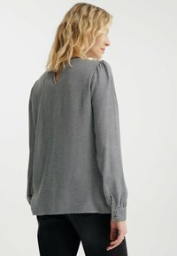 Zwart-wit geblokte blouse met lange mouwen, voorzien van een sleutelgaatje aan de achterkant, bijeen geraapte schouderaccenten en knoopmanchetten.
