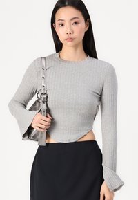 Szürke bordázott, hosszú ujjú felső, harangujjakkal; egy fekete szoknyával párosítva. A modell egy fémes kézitáskát tart, ezüst pánttal.