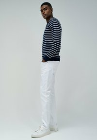 Maglione a righe blu navy e bianco con collo a giro, abbinato a jeans skinny bianchi e sneakers bianche. Caratterizzato da un design minimalista.