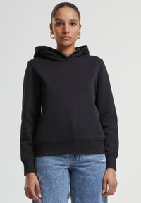 Sweatshirt à capuche noire avec une taille ajustée, des manches longues et une texture douce, associé à un jean délavé bleu clair.
