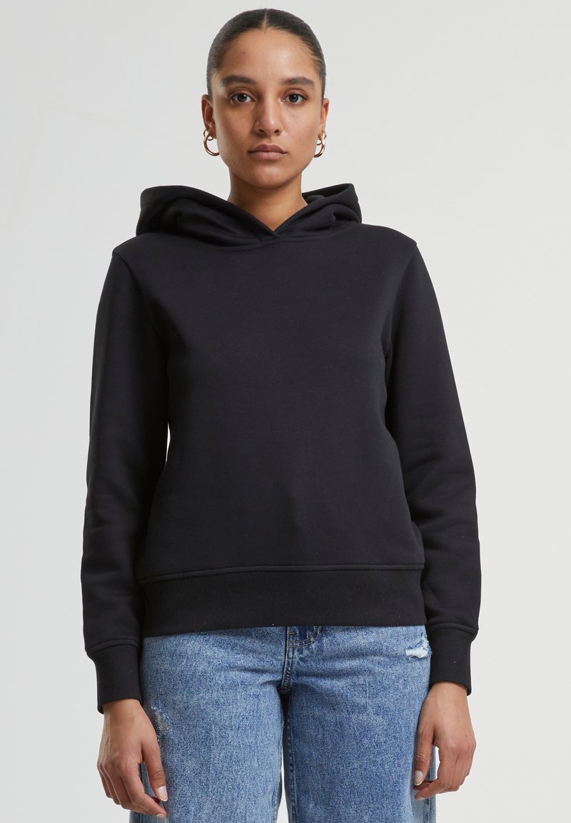 Sweatshirt à capuche noire avec une taille ajustée, des manches longues et une texture douce, associé à un jean délavé bleu clair.
