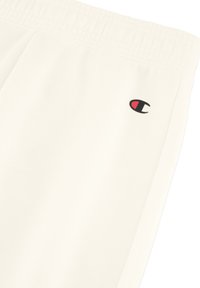 Crème-kleurige joggingsbroek met een elastische tailleband, een zachte textuur en een klein zwart en rood logo op de linkerdij.
