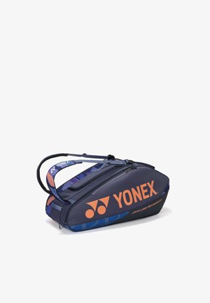 Marineblauwe en blauwe Yonex sporttas met oranje logo, draagriemen en meerdere met rits afgesloten vakken, ontworpen voor het opbergen van rackets.