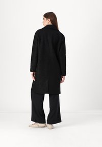 Cappotto di lana nero con colletto, maniche lunghe e taglio dritto. Caratterizzato da un tessuto testurizzato, design di lunghezza media e un'apertura centrale sul retro.