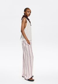 Top sans manches gris clair et pantalon ample rayé rouge et blanc. Présente un foulard en crochet brun au niveau du cou et des sandales noires.