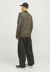 Pull en mailles texturées marron avec un col noir, associé à un pantalon noir ample et des baskets noir et blanc, vu de dos.