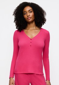 Roze langetermijn top met een V-hals, voorzien van een knoopsluiting en geribbelde textuur. Glad materiaal, aansluitende pasvorm en casual stijl.