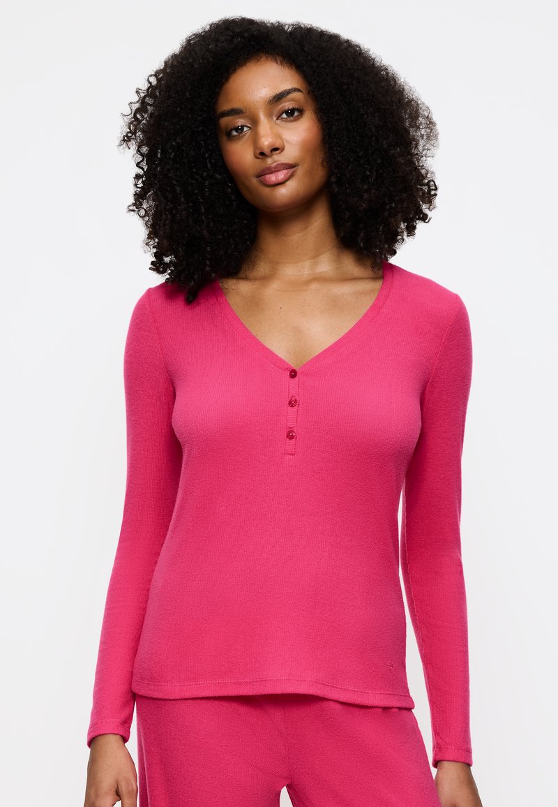 Roze langetermijn top met een V-hals, voorzien van een knoopsluiting en geribbelde textuur. Glad materiaal, aansluitende pasvorm en casual stijl.