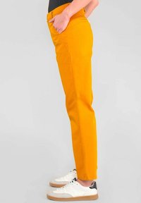 Gelbe Baumwollhosen mit slim fit, ausgestattet mit Seitentaschen und umgeschlagenen Säumen, kombiniert mit weißen Sneakers und einem schwarzen Top.