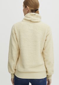 Cream-colored fleece pullover with a high collar, textured fabric, and contrasting ribbed cuffs and hem, showcasing a relaxed fit.