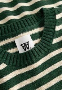 Pull en maille rayé vert et crème avec un col côtelé et une étiquette de marque blanche cousue à l'intérieur de l'encolure.