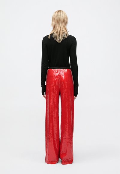 Pantalons larges en sequins rouges avec une texture brillante, assortis à un haut noir à manches longues, vus de dos sur fond blanc.
