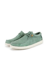 Zapatos de ante verde con punta redonda, cordones en la parte delantera y suela de goma blanca. Presentan un pequeño adorno de madera cerca de los cordones.