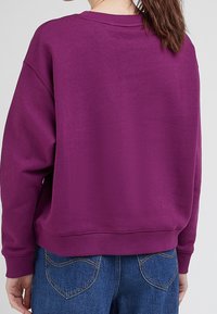 Purple oversized sweatshirt made of soft fabric; features ribbed cuffs and waistband, with a rounded neckline and a relaxed fit.