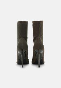 Stivali alla caviglia verde oliva con tomaia in tessuto elasticizzato, punta affusolata e alto tacco a stiletto. I dettagli delle cuciture aggiungono una sottile texture.