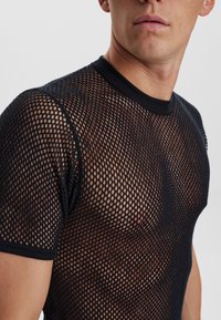 Sort mesh top med korte ærmer og rund hals; har en grid-lignende tekstur og en tætsiddende silhuet, der fremhæver huden under stoffet.