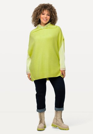 Limonengrüner oversized Pullover mit einem Kragen-Halsausschnitt, gestreiften Ärmeln, kombiniert mit dunkelblauen Jeans und beigen Schnürstiefeln mit grünen Sohlen.