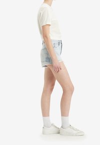 Pantalones cortos de mezclilla azul claro con dobladillo deshilachado, combinados con una camiseta blanca de manga corta y zapatillas blancas con suelas de goma texturizadas.