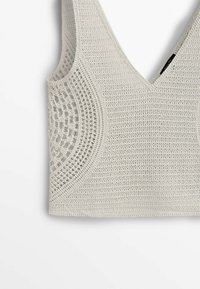 Beżowy crop top na szydełku z dekoltem w serek, grubymi ramiączkami i okrągłym wzorem koronkowym po bokach na białym tle.