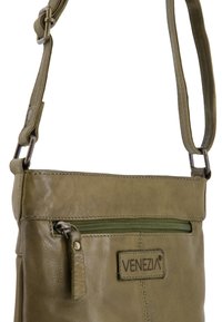 Olivgrüne Leder-Crossbody-Tasche mit glatter Textur, ausgestattet mit einem Reißverschlussfach und einem Logo-Tag. Verstellbarer Trageriemen und metallische Hardware-Akzente.