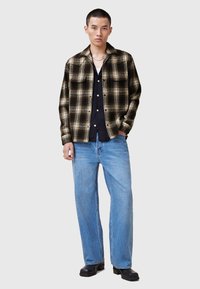 Sort og brun plaidskjorte, knaplukket, med to brystlommer over en sort top, parret med lyseblå vide jeans og sorte støvler.