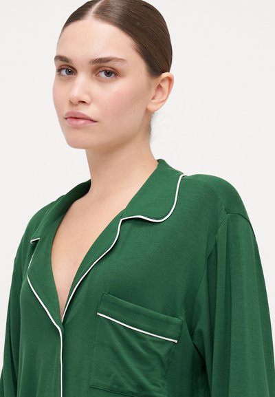 Green pajama top made from soft fabric, featuring a notch collar, white piping, and a single pocket on the left side.