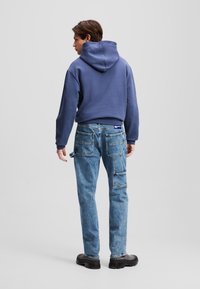 Sweatshirt com capuz azul marinho com um corte descontraído, combinado com calças de ganga cargo azul claro que apresentam múltiplos bolsos e um design de perna reta.