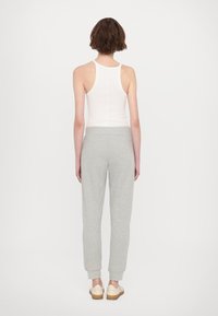 Witte mouwloze top en lichtgrijze joggingsbroek met elastische boorden. De joggers hebben een zachte textuur en een relaxte pasvorm.