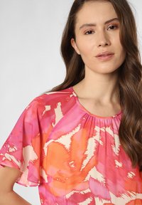 Fließende Bluse in Schattierungen von Rosa und Orange mit einem abstrakten Muster. Sie hat einen runden Halsausschnitt und schneckenförmige Ärmel aus leichtem Stoff.