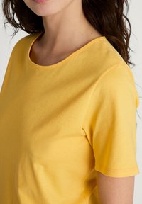 Geel t-shirt met korte mouwen, gemaakt van een zachte stof, met een ronde hals en subtiele ribbels aan de kraag en mouwranden.