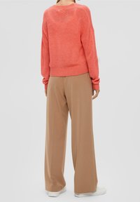 Jasnoróżowy, oversize'owy sweter koralowy z prążkowanymi mankietami i obrębem, zestawiony z beżowymi, szerokimi spodniami i białymi trampkami. Miękka faktura, swobodny krój.