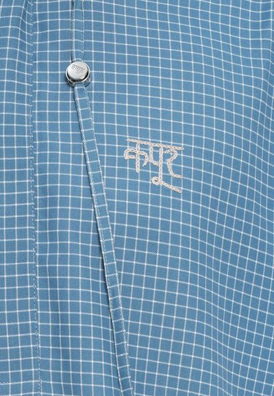 Camisa a cuadros azul con pequeños cuadrados blancos, que presenta un botón a presión de metal y texto bordado en blanco. Tejido suave con una textura lisa.
