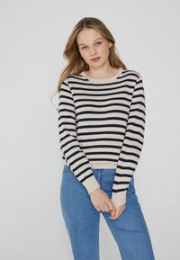 Sweter w paski w kolorze kremowym i granatowym, z okrągłym dekoltem i długimi rękawami z ribbowanymi manszetami, w połączeniu z niebieskimi dżinsami.
