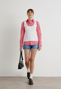 Hvit, ribbestrikket tank topp over en rød og hvit stripete skjorte med knapper, kombinert med blå denimshorts, svarte klumpete sko og en liten svart veske.