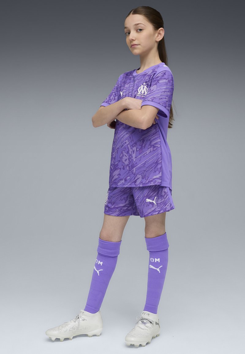 Completo da calcio viola con maglia a fantasia e pantaloni abbinati, completato da calzettoni coordinati. Include dettagli in bianco per il logo e scarpe argentate.