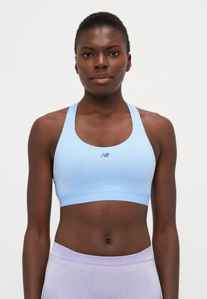 Sport bra di colore blu chiaro con un design aderente, realizzato in tessuto liscio. Presenta un collo rotondo e un piccolo logo viola sul davanti.