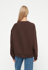 Sweatshirt marron oversize avec un col rond, des manches raglan, des poignets et un ourlet côtelés, présenté de dos avec un jean baggy.