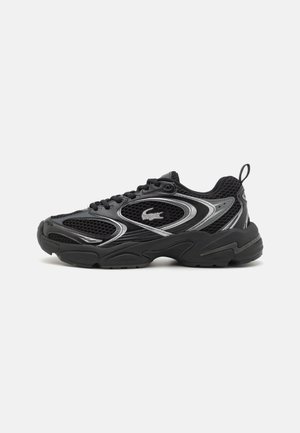 Czarny sportowy sneaker z panelami z siateczki, grubą podeszwą, wiązaniem na sznurówki, srebrnymi akcentami i logo krokodyla po boku.