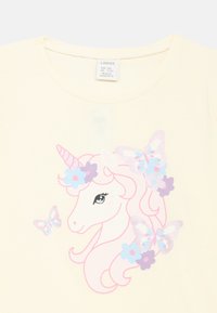 Camiseta de manga corta color amarillo claro con un unicornio estampado con cabello rosa, detalles florales y mariposas de colores. Material de algodón suave.