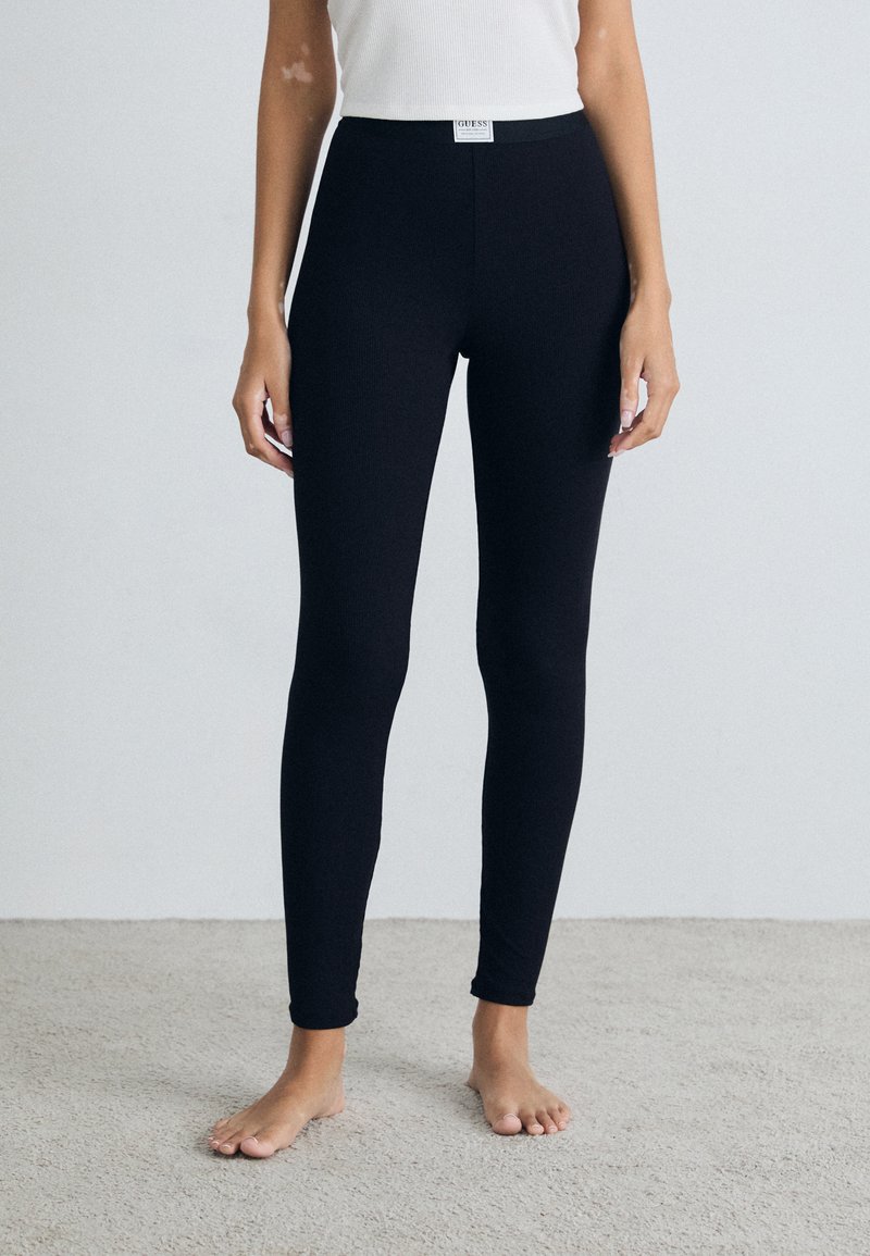 Black leggings with a stretchy fabric and a high waistband, featuring a logo tag at the front. They have a smooth, fitted design.