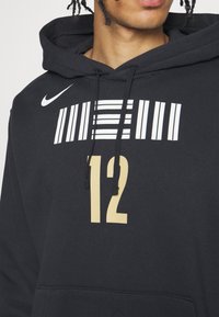 Felpa nera con cappuccio realizzata in morbido tessuto strutturato, decorata con una grafica bianca con strisce orizzontali e il numero "12" in oro. Dotata di tasca a marsupio.