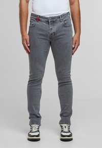 Vaqueros de mezclilla gris con un diseño ajustado, cinco bolsillos y un acento rojo en la cintura. Llevados con zapatillas negras y blancas.