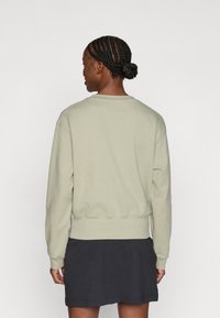 Φωτεινό πράσινο φούτερ από μαλακό ύφασμα με ριμπ μέση και μανσέτες, διαθέτοντας κλασικό σχέδιο με στρογγυλή λαιμόκοψη. Φορεμένο με μια σκούρα φούστα.