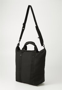 Črna torba z ročkami, izdelana iz trpežnega materiala, pravokotne oblike. Ima kratke ročaje in snemljivo naramnico. Gladka tekstura.