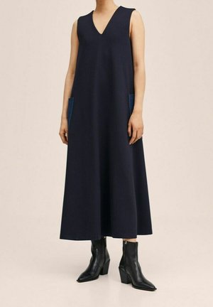 Navy ärmelloses Kleid mit V-Ausschnitt, ausgestattet mit zwei seitlichen Taschen aus blauen Denim. Glatte Textur, knöchellang, kombiniert mit schwarzen Stiefeletten.