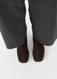 Brown suede ankle boots with a smooth finish, square toes, and minimalistic design, paired with dark cropped trousers.